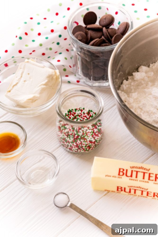Various ingredients laid out on a table: softened butter, a bowl of colorful sprinkles, vanilla extract, cream cheese, chocolate melting wafers, and powdered sugar, all prepped for the recipe.