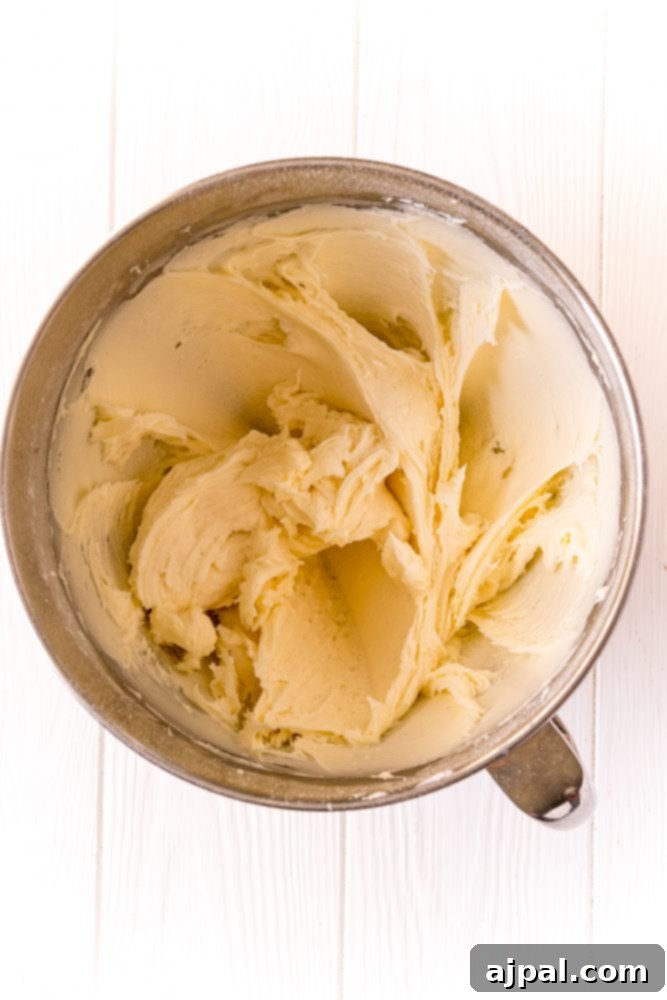 A lush mixture of powdered sugar, butter, cream cheese, and vanilla, all expertly creamed together in the bowl of a stand mixer, ready for the next step.