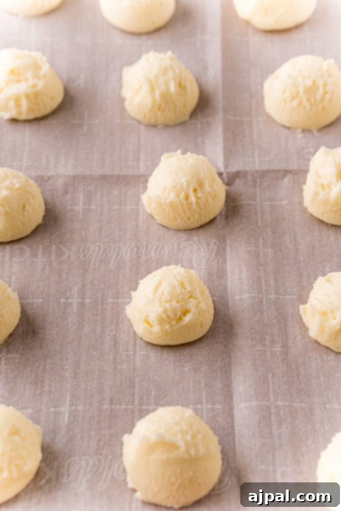 Small, perfectly formed balls of creamed butter, sugar, and cream cheese, neatly arranged on a baking sheet lined with parchment paper, chilling before their chocolate bath.