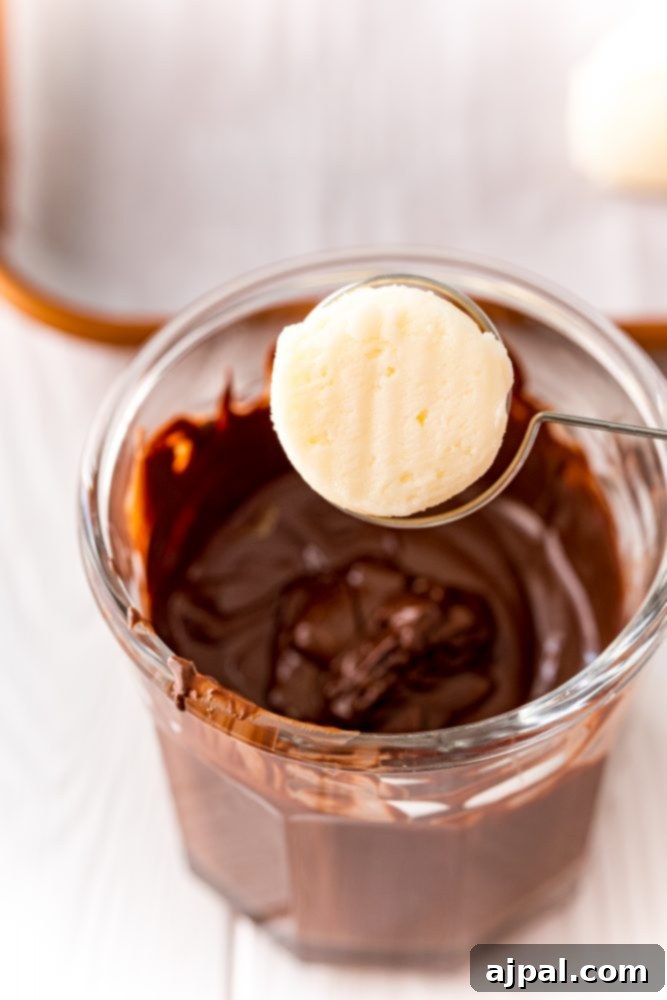 A single buttercream ball delicately balanced on a dipping fork, poised over a bowl of rich, melted chocolate, ready for its luxurious coating.