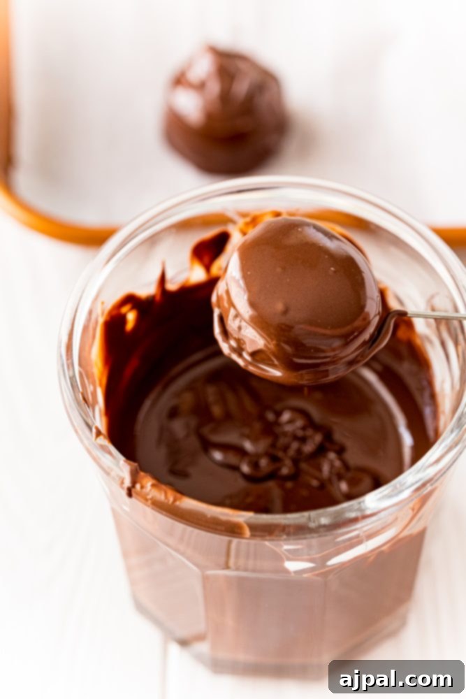 A delectable buttercream candy ball, now fully covered in a smooth layer of melted chocolate, held aloft by a dipping fork, showcasing its perfect coating.