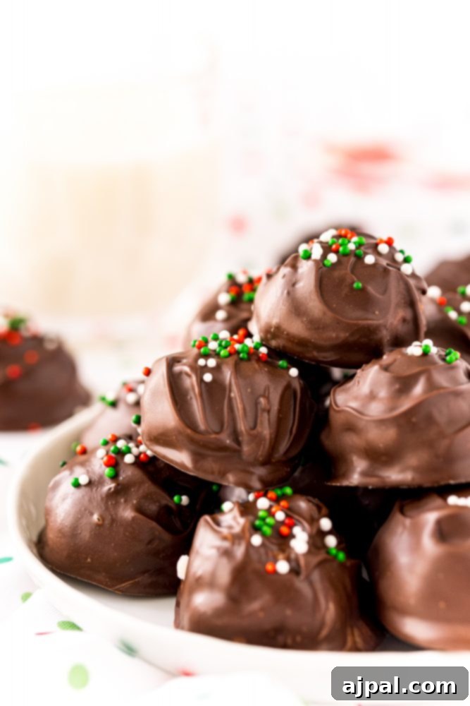 A delightful stack of chocolate-covered buttercream candy balls, adorned with vibrant green, white, and red sprinkles, presented invitingly on a pristine white plate.