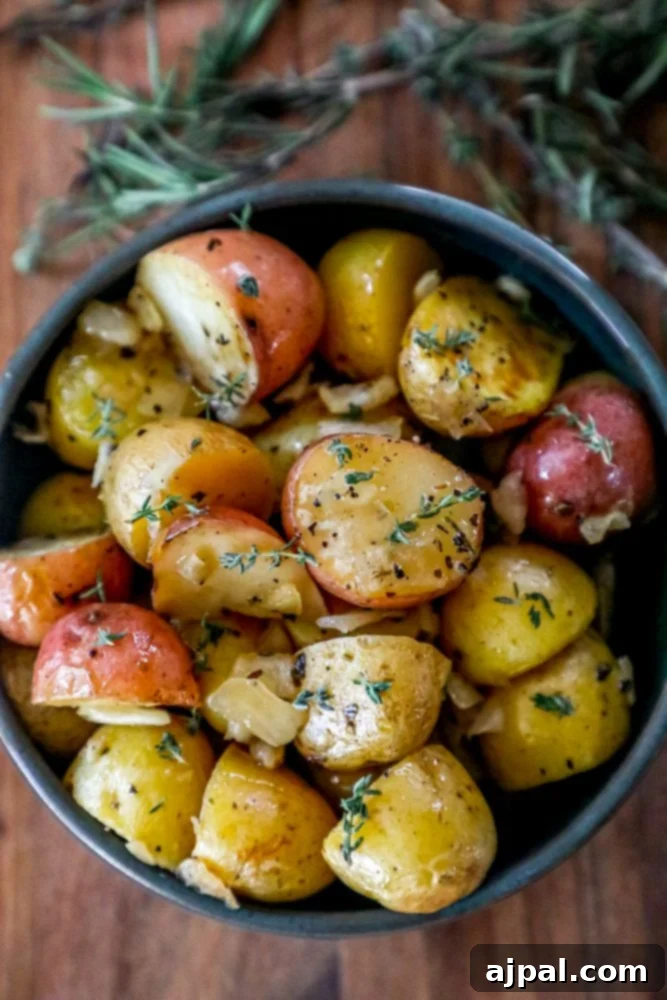 Crispy garlic butter roasted potatoes in a bowl, garnished with fresh herbs and a pat of melting butter.