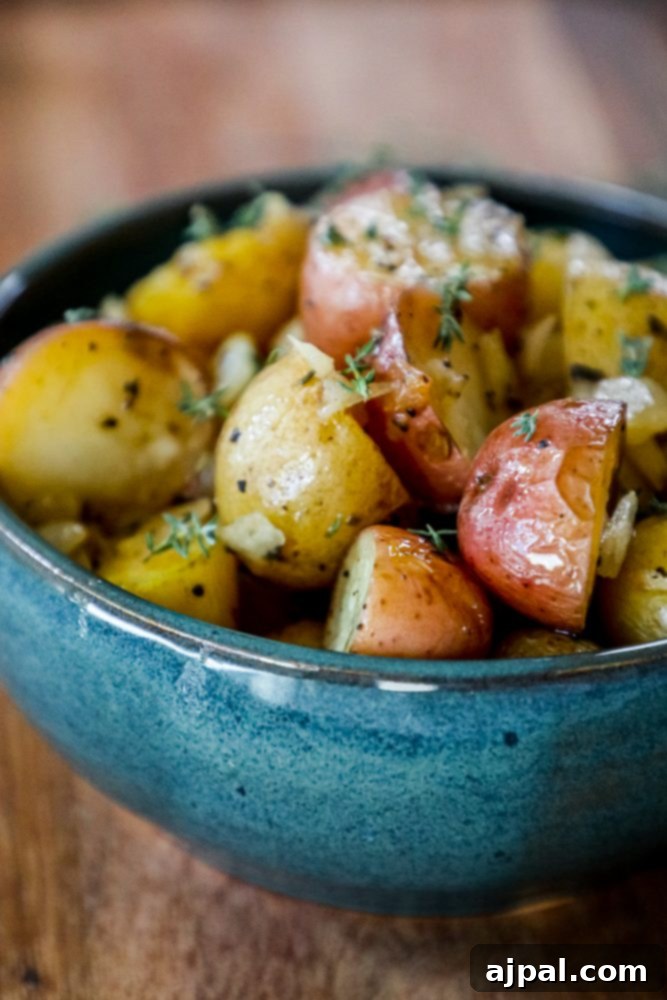 Close-up of butter roasted potatoes with fresh thyme in a rustic blue bowl, showcasing their golden crispiness.