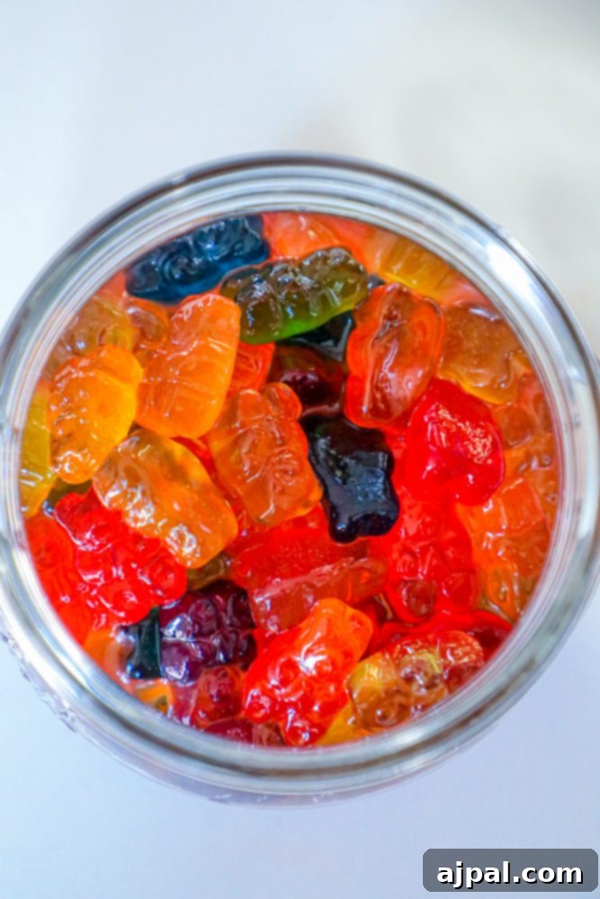A glass jar filled with gummy bears visibly soaking in a liquid, resting on a rustic wooden surface.