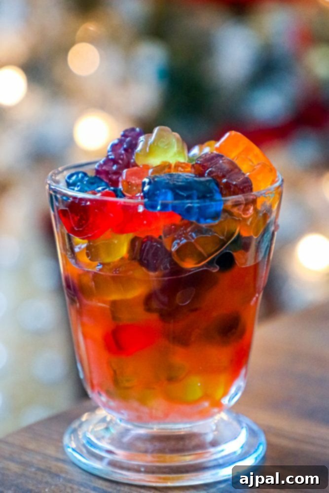 A tall glass filled with glistening Negroni gummy bears, with festive, blurred lights of a Christmas tree in the background, creating a cozy ambiance.