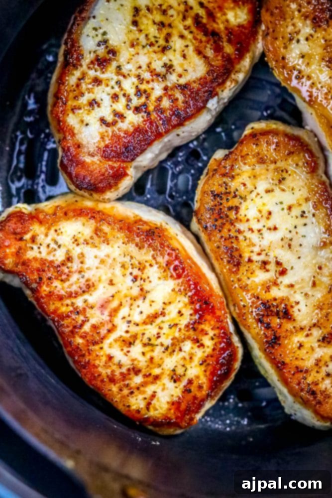 Picture of perfectly cooked pork chops resting in an air fryer basket, showcasing their golden-brown crust and juicy appearance.