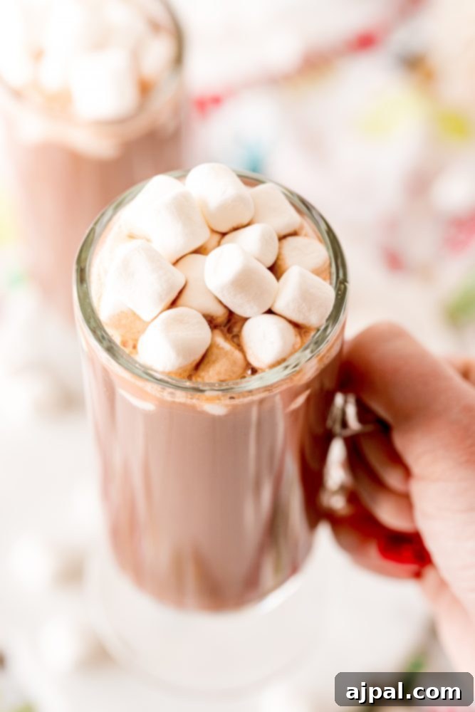Creamy Rumchata Hot Chocolate Cocktail 3 A person warmly holding a mug of luscious hot cocoa, topped with a generous swirl of marshmallows, enjoying a moment of boozy comfort.