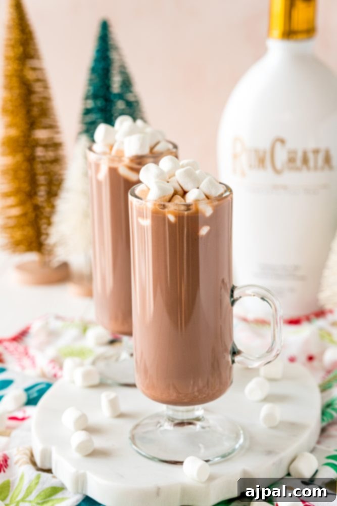 Creamy Rumchata Hot Chocolate Cocktail 4 Tall glasses brimming with hot chocolate and marshmallows are artfully arranged, with a distinctive RumChata bottle gracefully positioned in the background, hinting at the key ingredient.