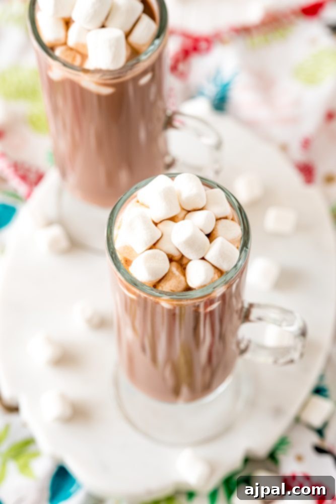 Creamy Rumchata Hot Chocolate Cocktail 5 Two enticing glasses of boozy hot cocoa, generously adorned with fluffy marshmallows, resting invitingly on a festive table setting.
