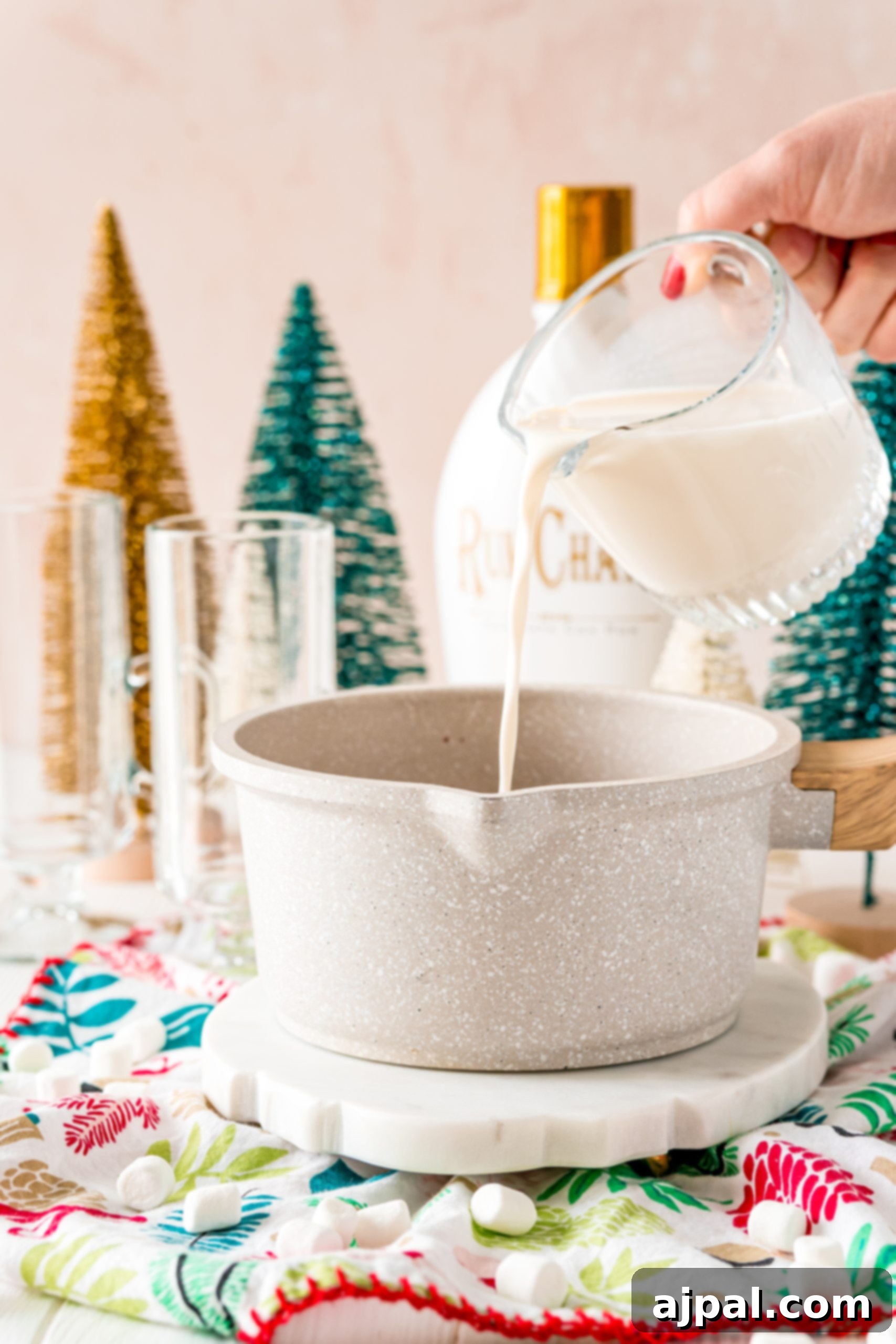 Creamy Rumchata Hot Chocolate Cocktail 6 A person making a festive Rumchata cocoa recipe by pouring milk into a pot on a Christmas table.