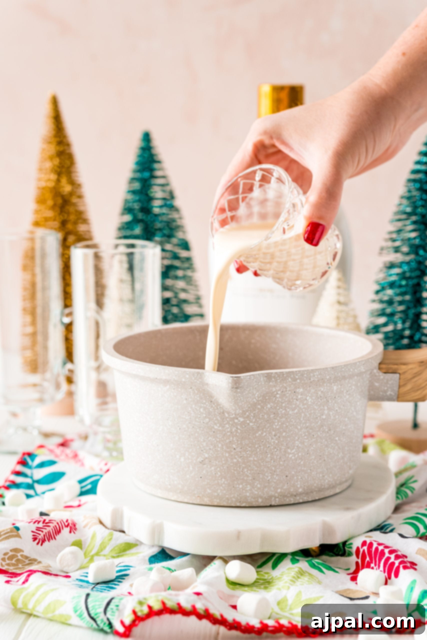 Creamy Rumchata Hot Chocolate Cocktail 7 A person pouring RumChata into a bowl on top of a Christmas tree.