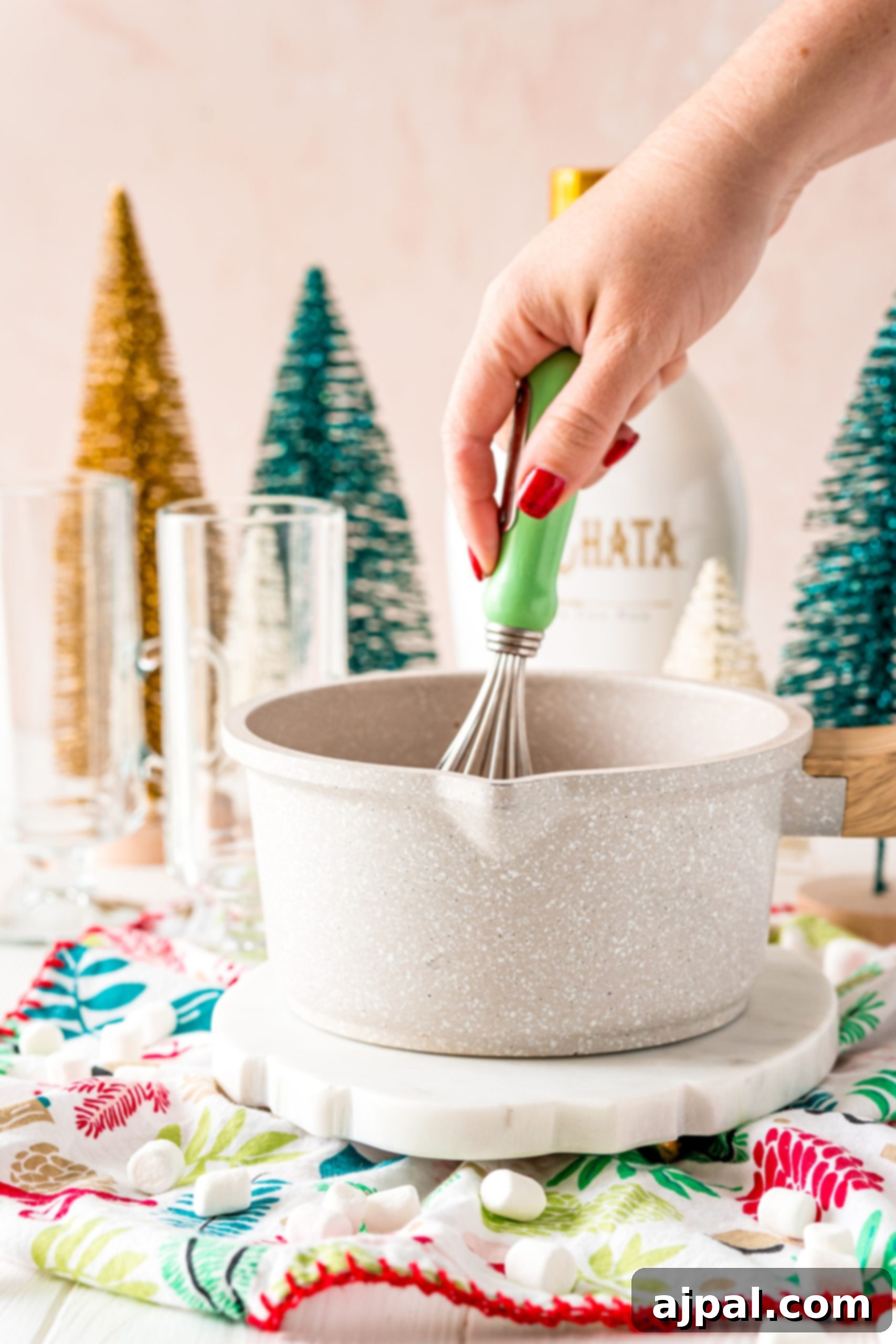 Creamy Rumchata Hot Chocolate Cocktail 9 A person preparing a Rumchata cocktail with Christmas tree decorations.