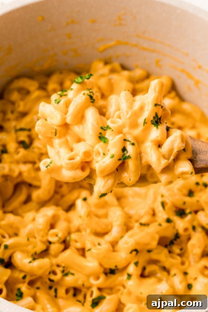 Creamy macaroni and cheese being stirred in a pot with a wooden spoon.