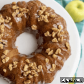 A beautifully baked bundt cake, crowned with chopped walnuts and glistening caramel glaze, presented on a white plate with fresh green apples nearby.