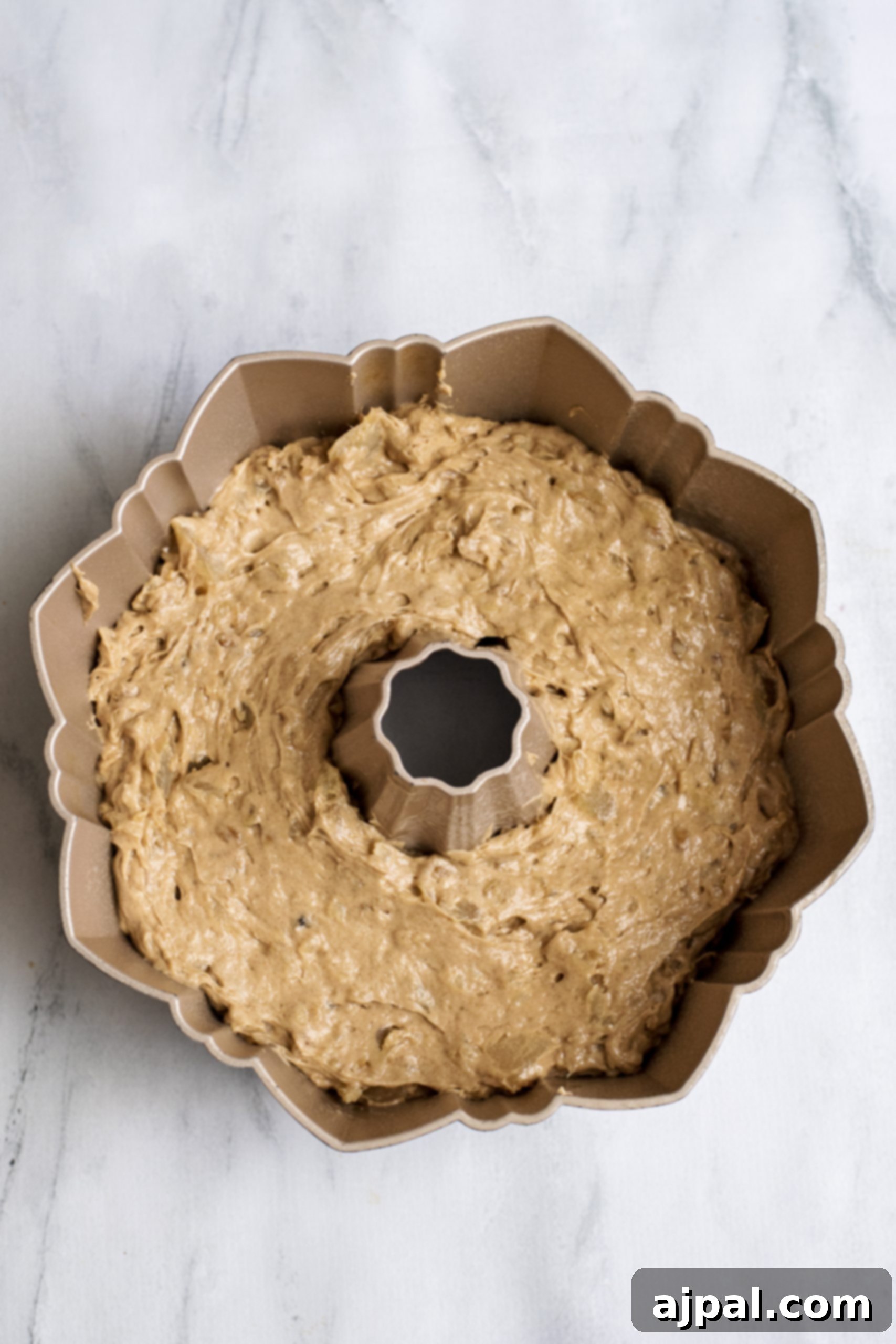 An apple spice bundt cake in its pan, freshly baked and resting on a marble countertop.