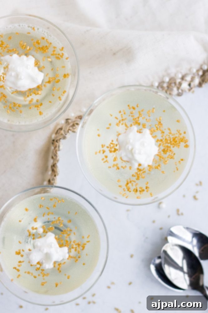 Two elegant champagne jello shots with a smooth, clear texture, each topped with a dollop of whipped cream and glistening gold sprinkles, showcasing their festive appeal.