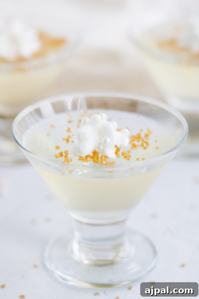 A clear glass of sparkling champagne jello shot, gracefully topped with a swirl of whipped cream and golden sprinkles, ready for a festive toast.
