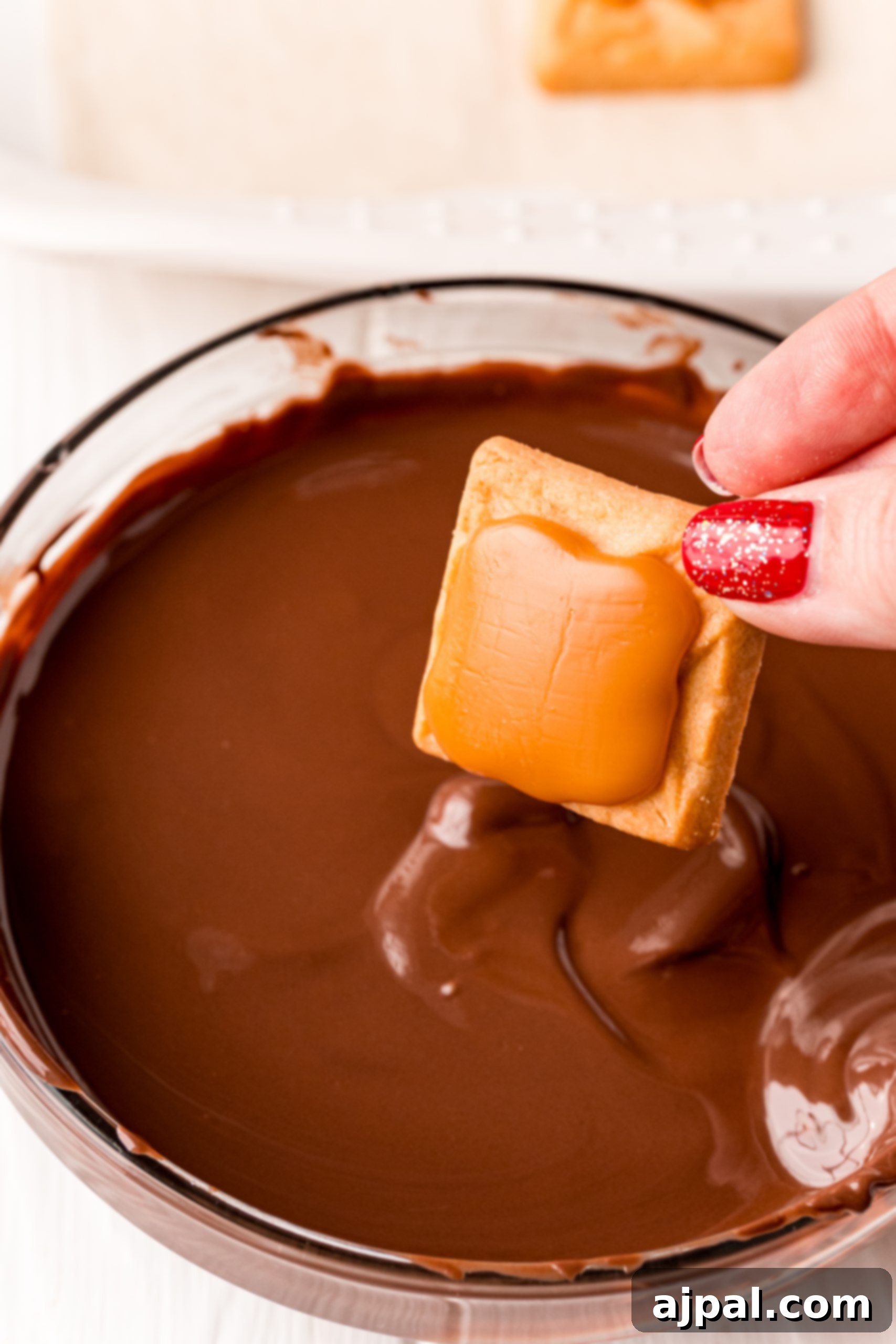 Decadent Millionaire Shortbread Bites Made Easy 12 A person expertly dipping a graham cracker into melted chocolate, part of the process for making an Easy Millionaire Shortbread Bites recipe.