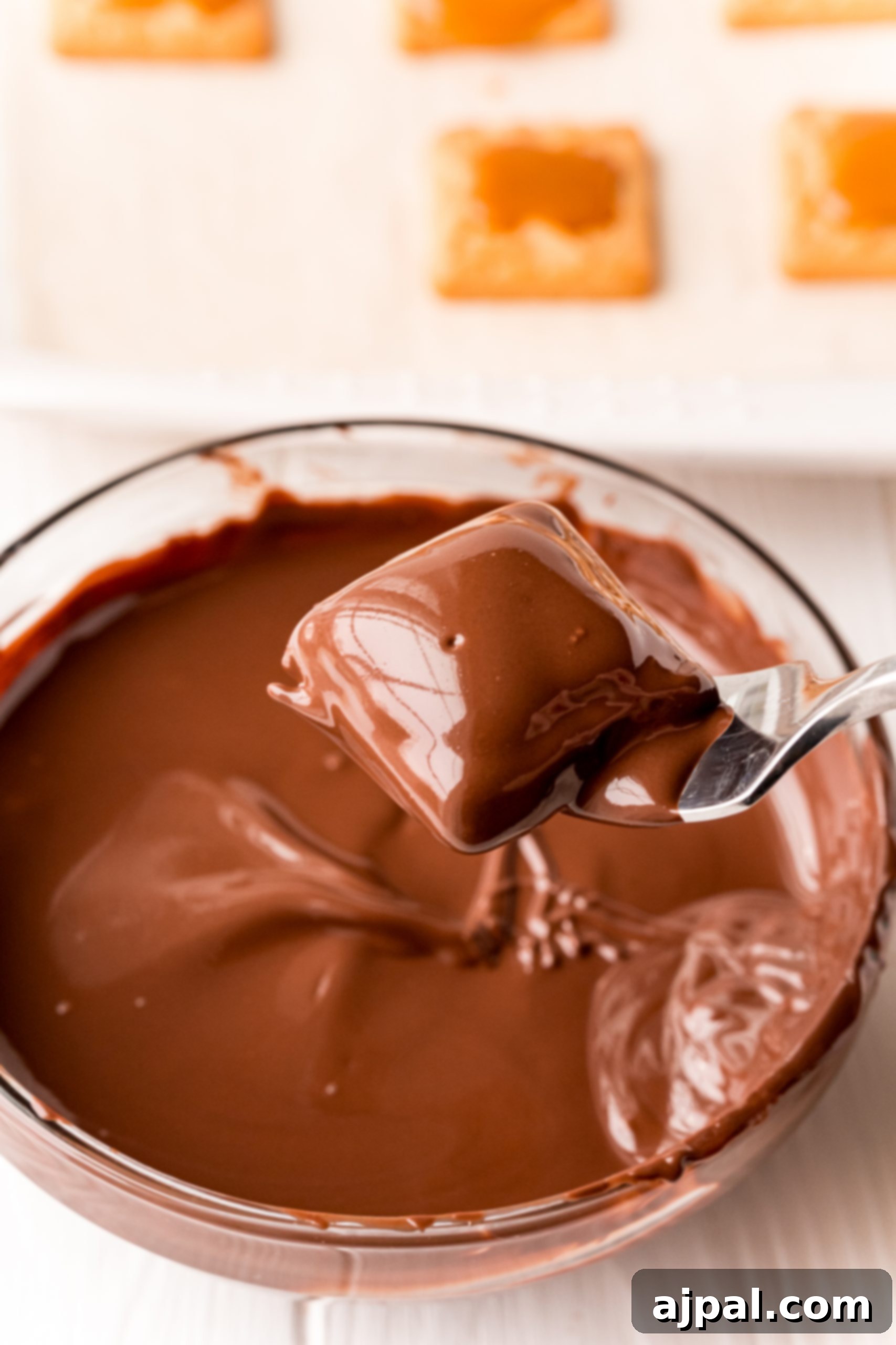 Decadent Millionaire Shortbread Bites Made Easy 13 A spoon expertly dips chocolate into a bowl filled with crisp crackers, illustrating a step in crafting an easy Millionaire Shortbread Bites recipe.