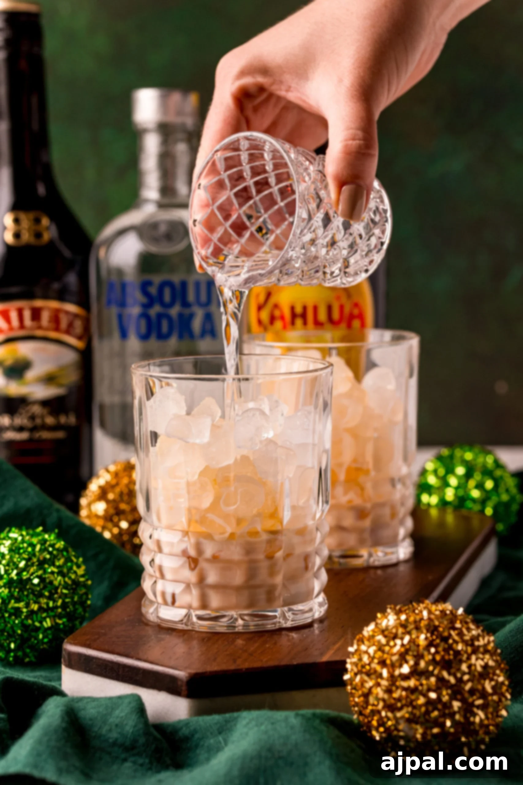 A clear glass filled with ice, as a person carefully pours a White Russian cocktail into it, showcasing the layering effect.