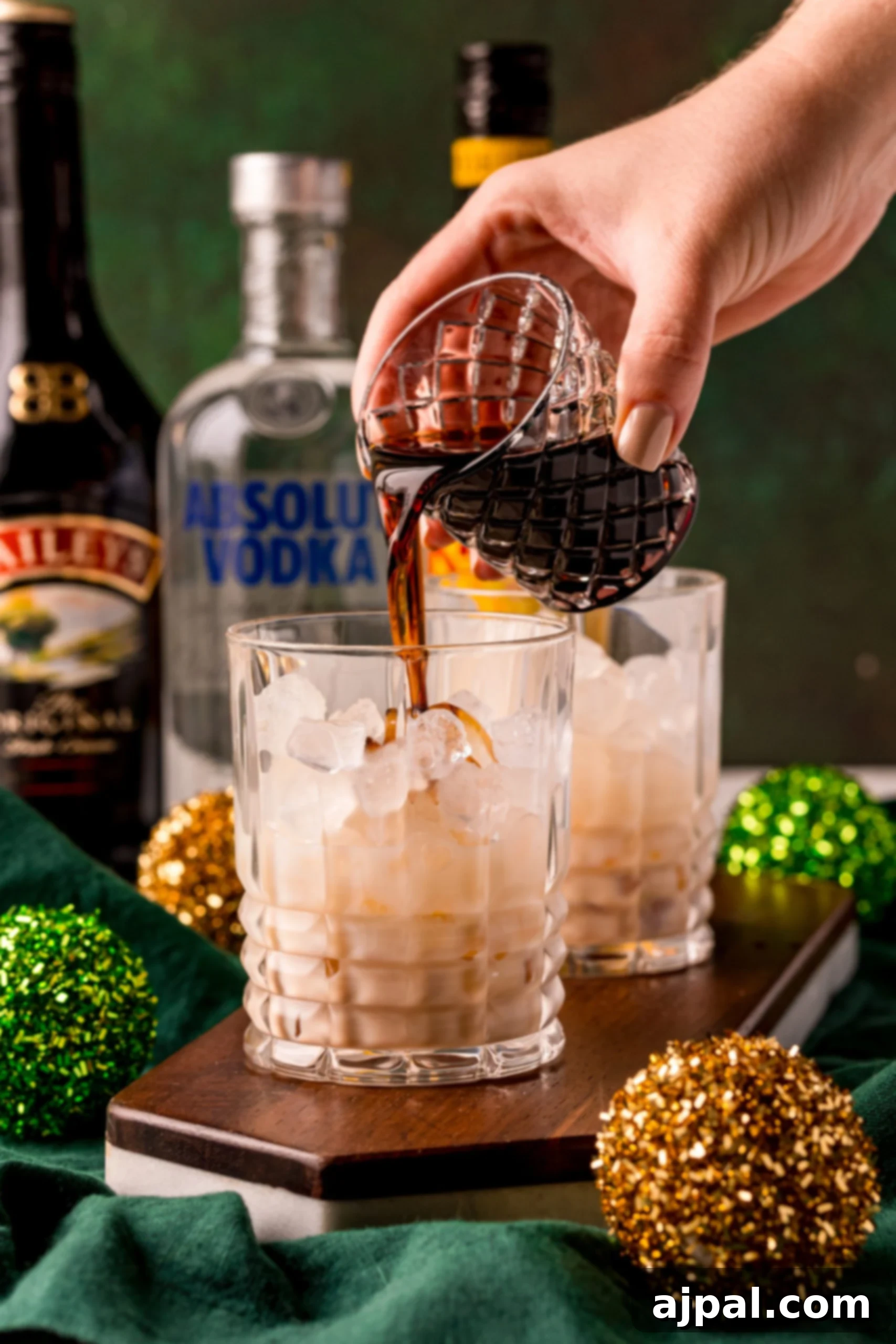 A hand pouring a rich Baileys White Russian cocktail into a waiting glass, emphasizing the creamy texture.