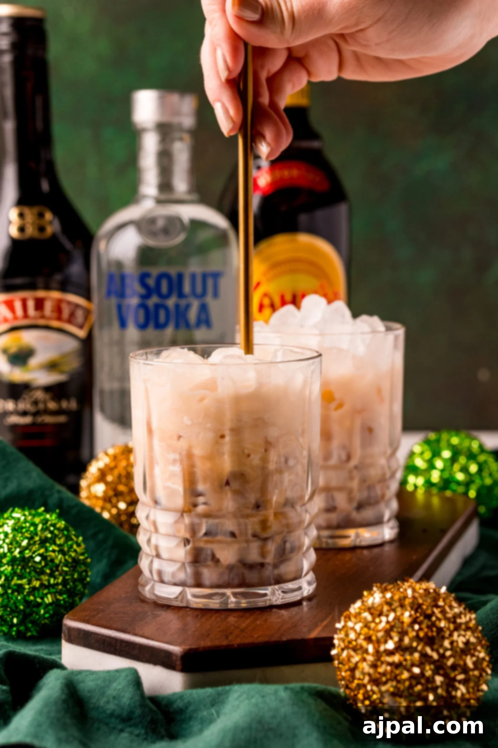 A hand gently stirring an Irish Cream White Russian in a glass, ensuring all ingredients are perfectly blended.