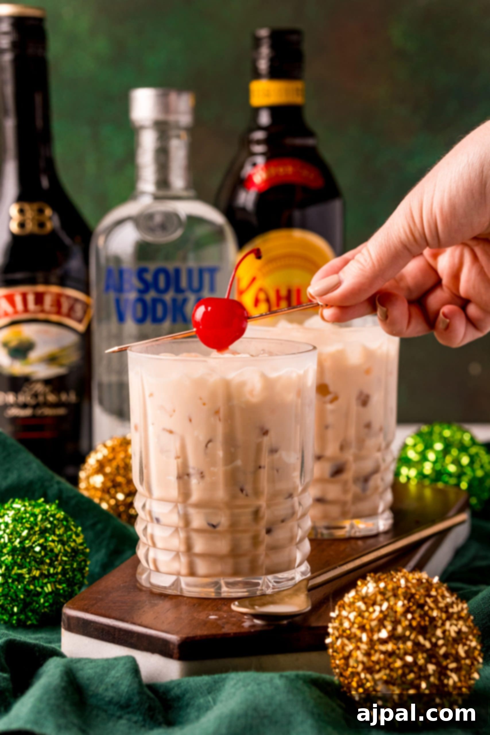 A hand holding a beautifully finished Irish Cream cocktail, complete with a bright cherry on top, ready for enjoyment.