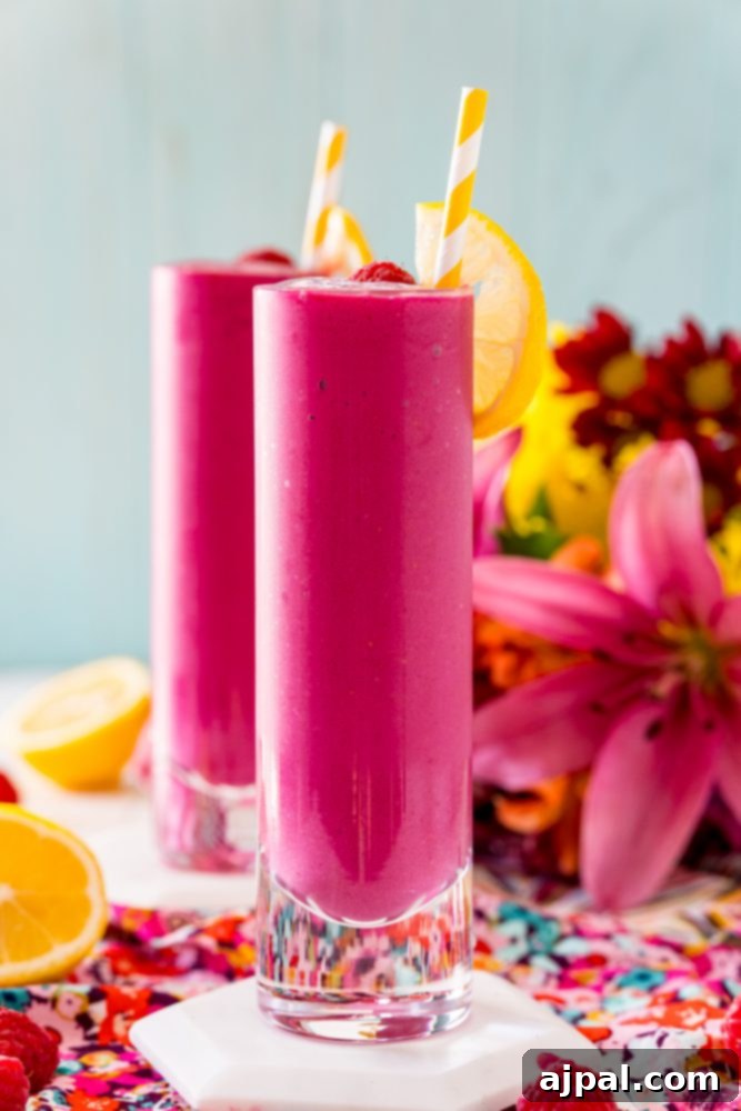 Vibrant Beet Raspberry Blend 2 Two glasses of bright pink Raspberry Beet Smoothie, garnished with fresh raspberries and a lemon slice.