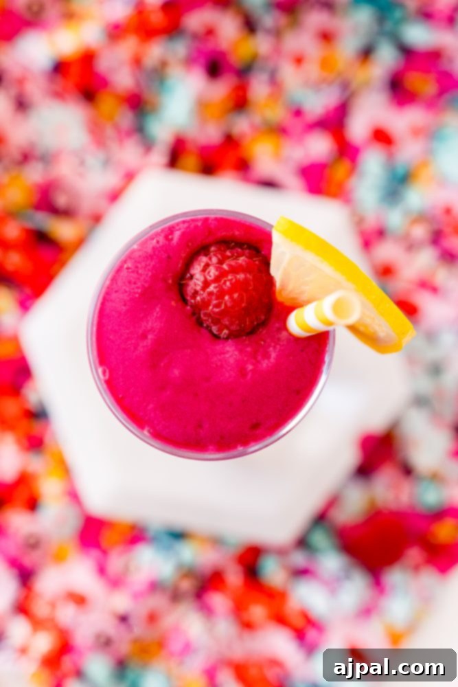 Vibrant Beet Raspberry Blend 6 A tall glass of pink raspberry beet smoothie, topped with a few fresh raspberries, sitting on a light surface.