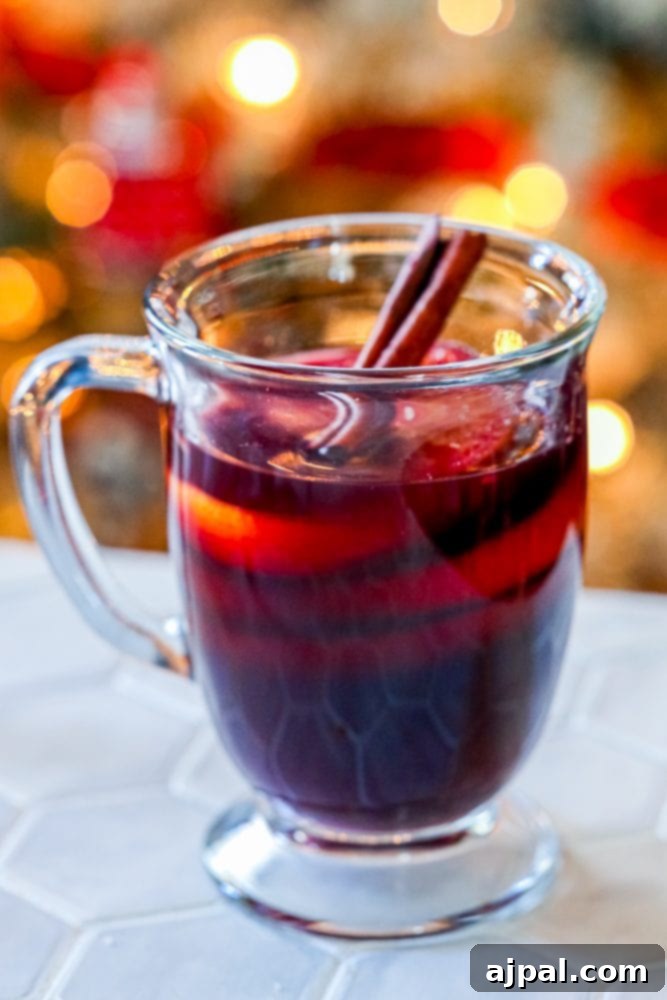 A festive mug of Flaming German Rum Punch, or Feuerzangenbowle, garnished with cinnamon sticks, rests on a table, ready to be enjoyed during holiday celebrations.