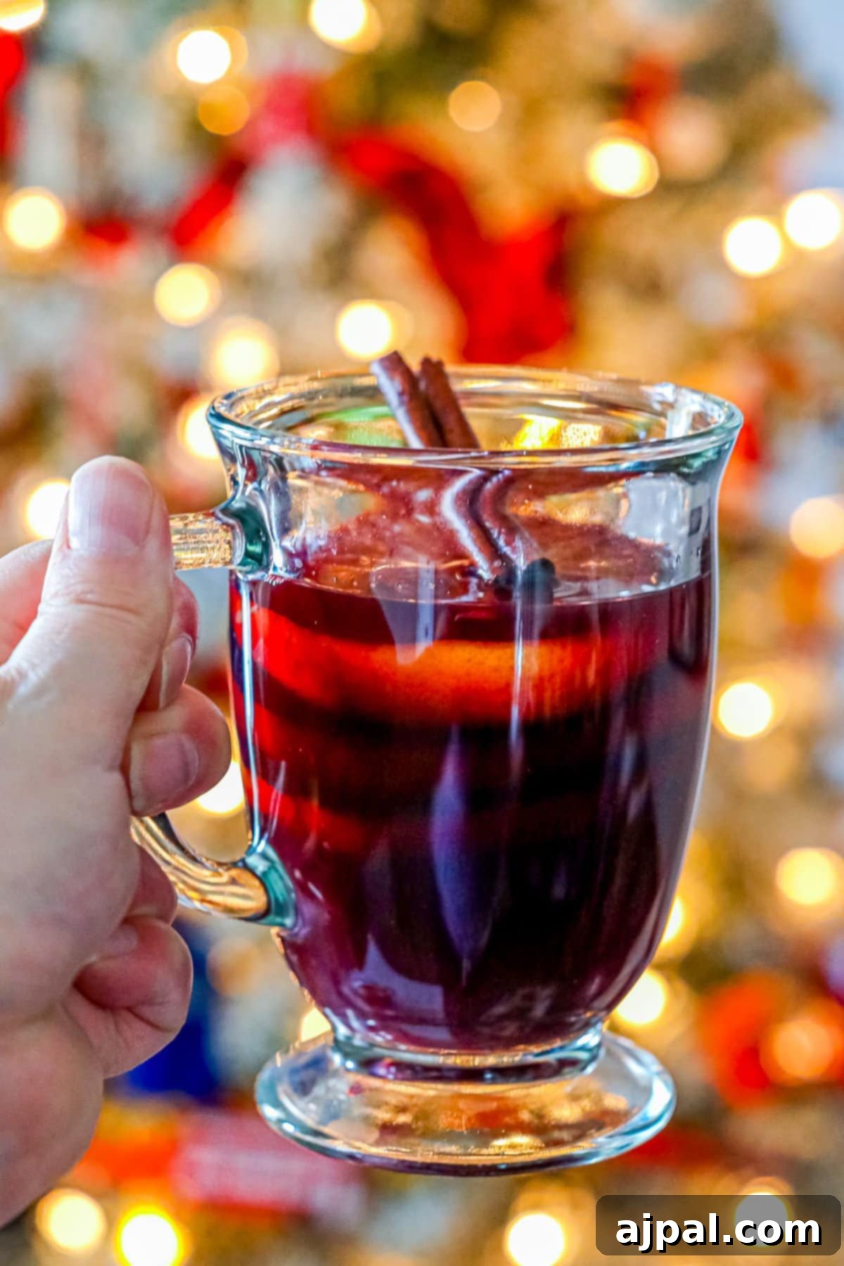 A person warmly holds a mug of Feuerzangenbowle, a fiery mulled wine, against the backdrop of a festive Christmas tree, embodying the cozy holiday spirit.