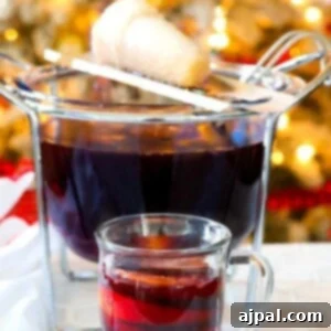 Feuerzangenbowle in a mug in front of a punch bowl with a sugar cone on fire over it
