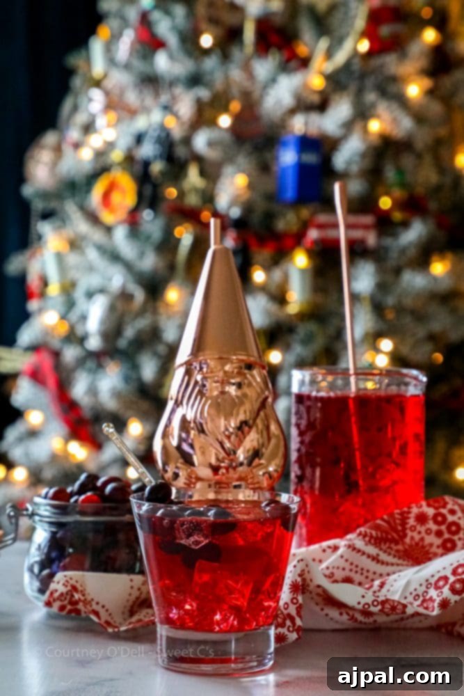 Ruby Cranberry Fizz 7 A glass of cranberry juice with fresh cranberries floating in it, set against a festive Christmas tree background, perfect for a holiday mocktail.