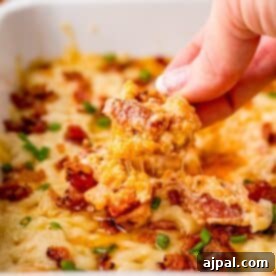 A person preparing a savory bacon and cheese dip by dipping a piece of bacon and cheese casserole into a dish.