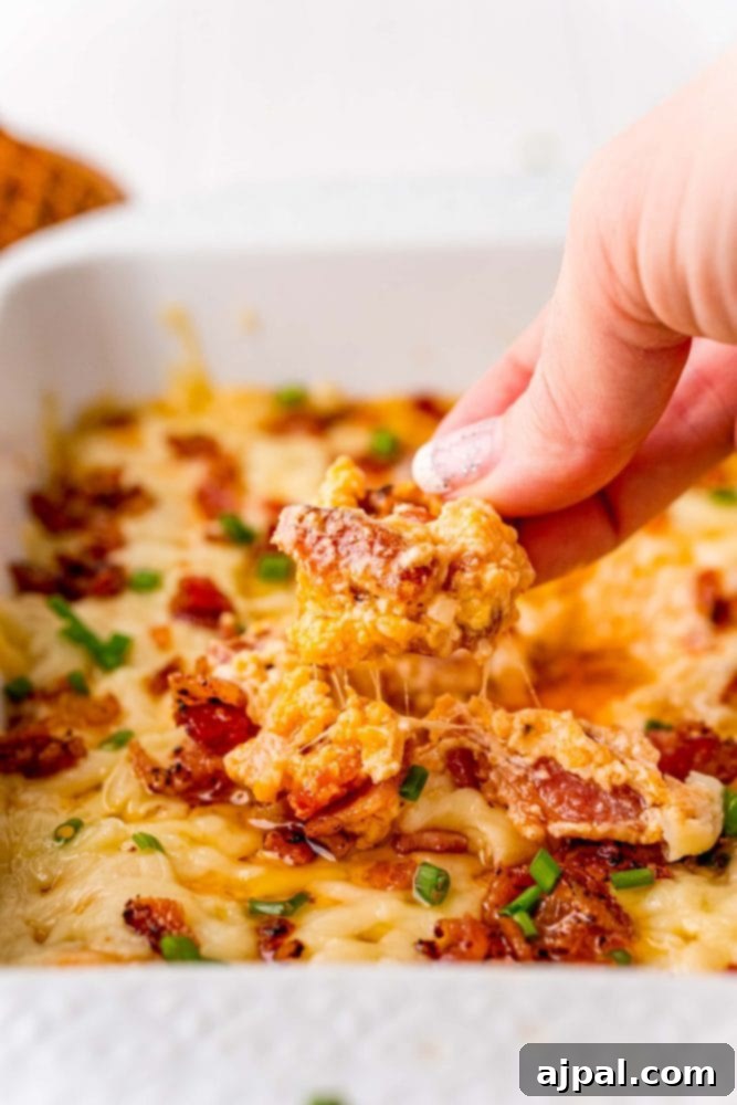 A person grabbing a piece of a bacon cheese dip casserole.