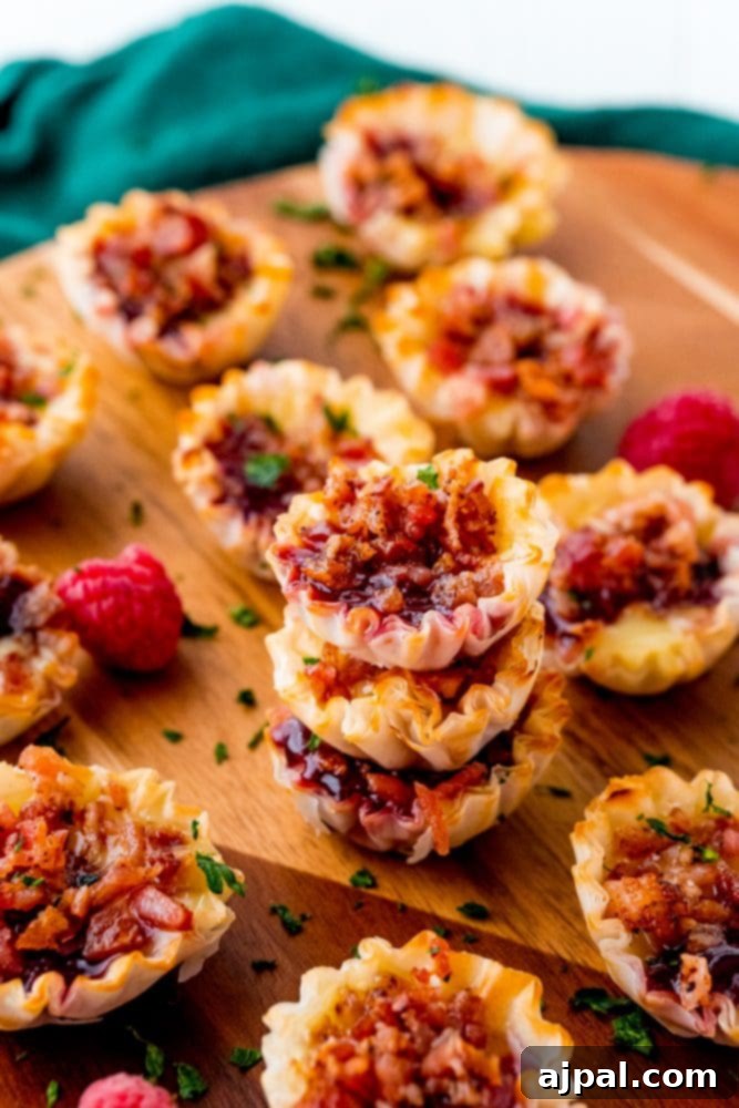 Cheesy Bacon Raspberry Morsels 13 A beautifully arranged stack of raspberry and bacon tart bites sits on a wooden cutting board, inviting guests to indulge in their sweet and savory flavors.