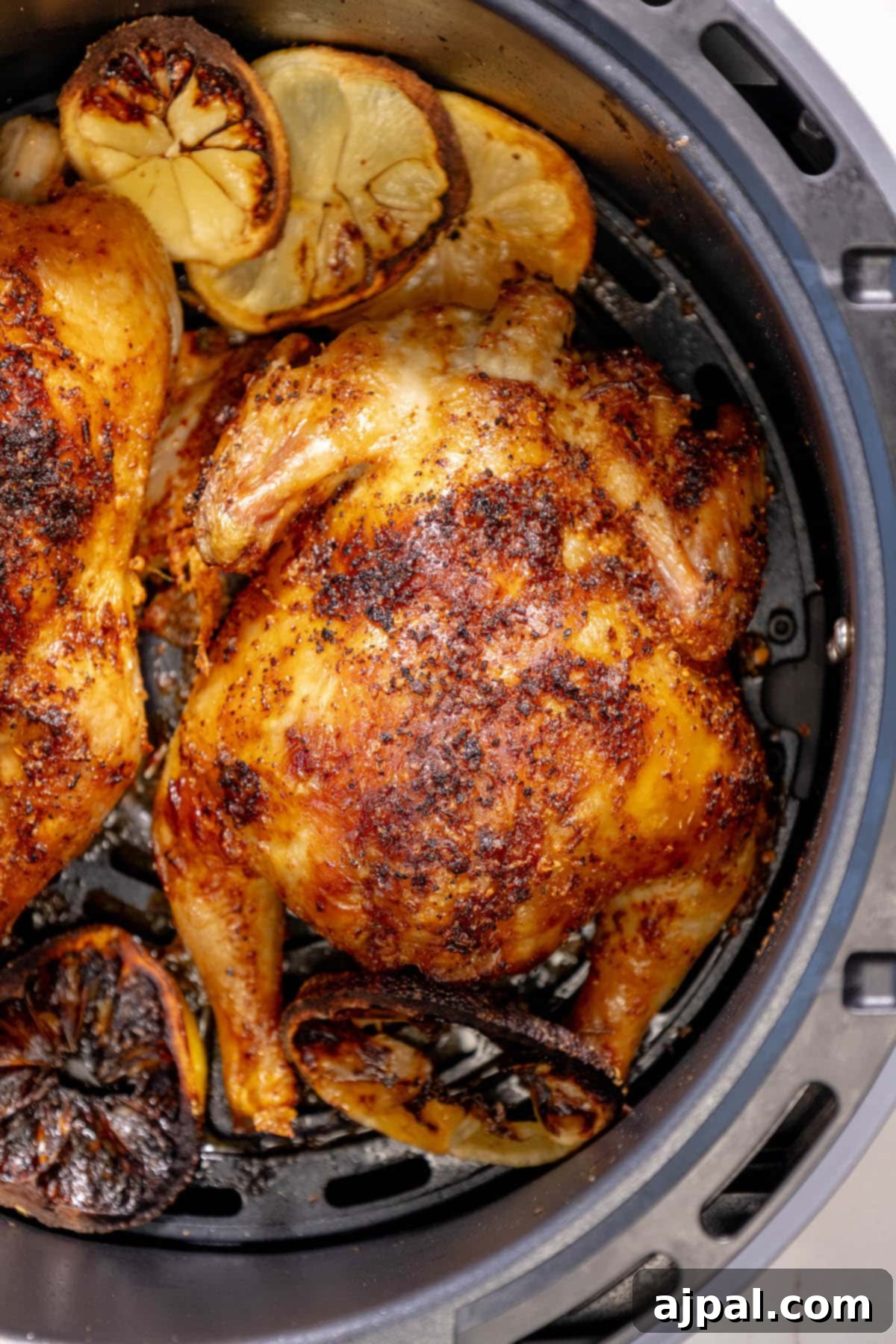 Golden Crispy Air Fryer Cornish Hen 3 Succulent air-fried Cornish game hens, beautifully seasoned with aromatic herbs, resting in an air fryer basket atop fresh slices of lemon.