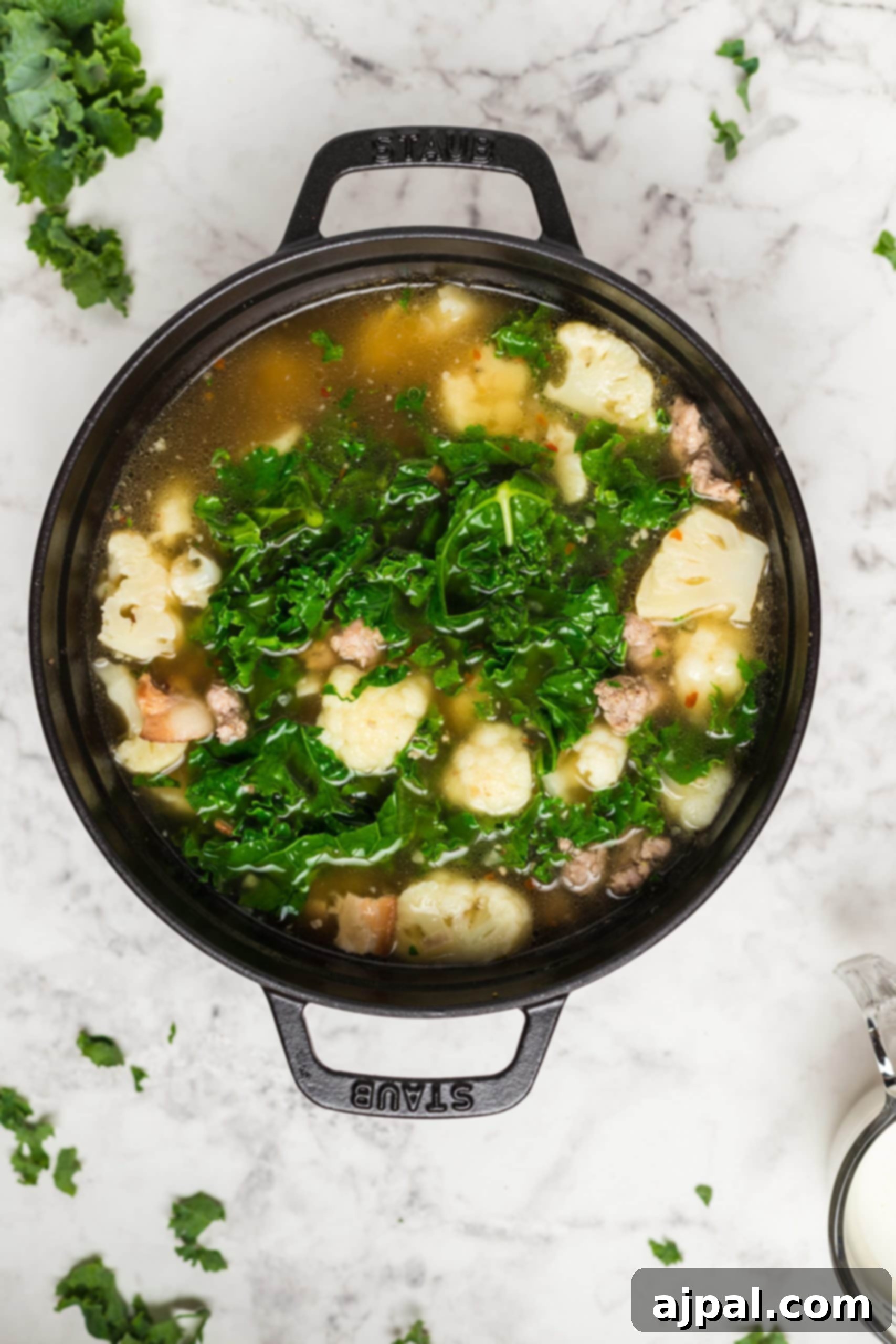 Simple Creamy Keto Tuscan Kale Soup 12 A generous serving of Keto Tuscan Kale Soup with sausage, fresh kale, and a creamy texture, on a marble table.
