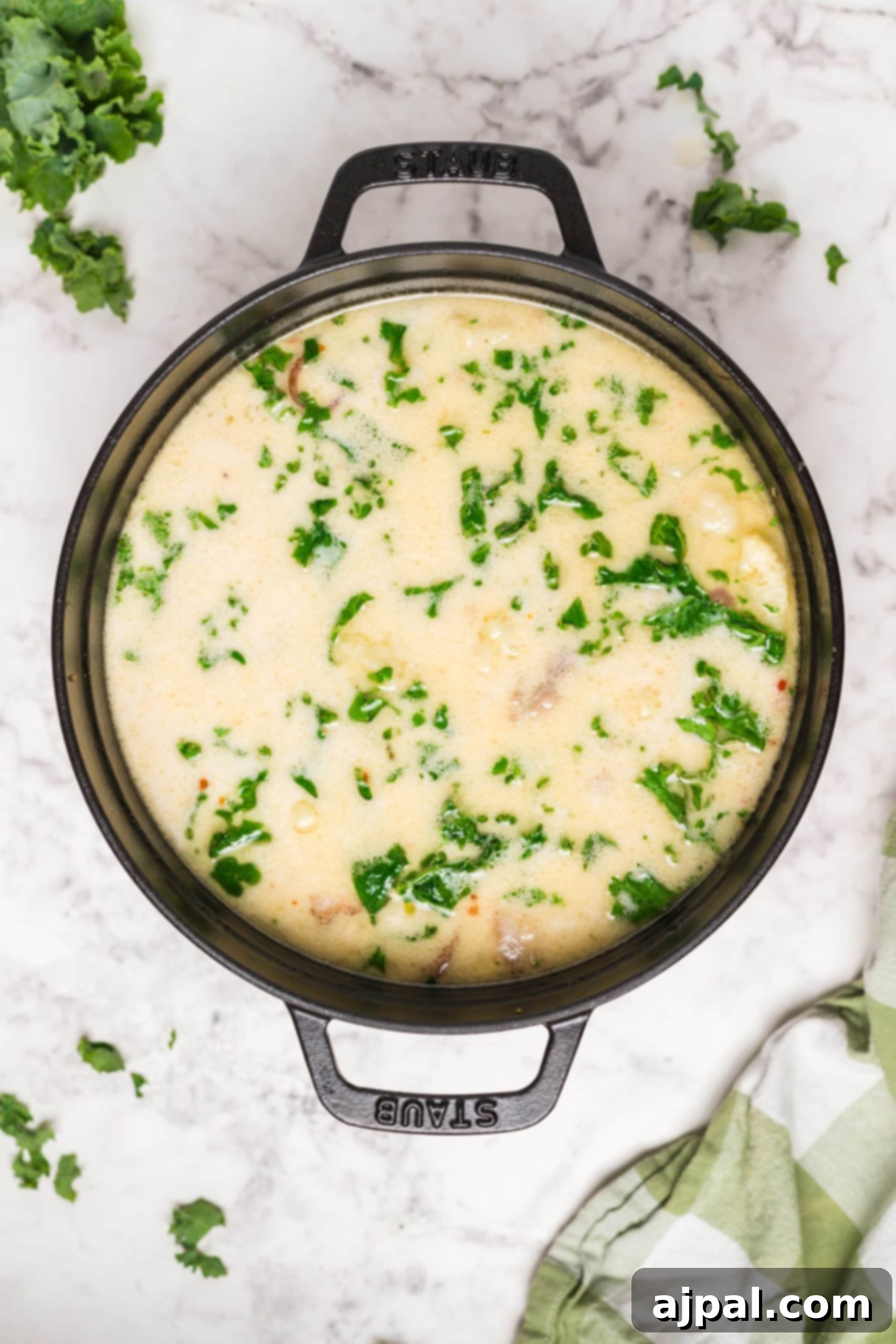 Simple Creamy Keto Tuscan Kale Soup 4 A Keto Tuscan Kale Soup garnished with fresh parsley and a sprinkle of Parmesan cheese on a marble surface.