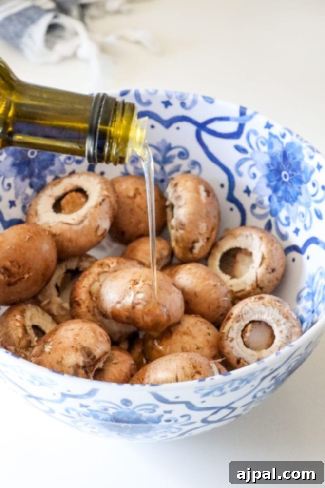 Olive oil being drizzled over fresh mushroom caps in a mixing bowl, preparing them for air frying.