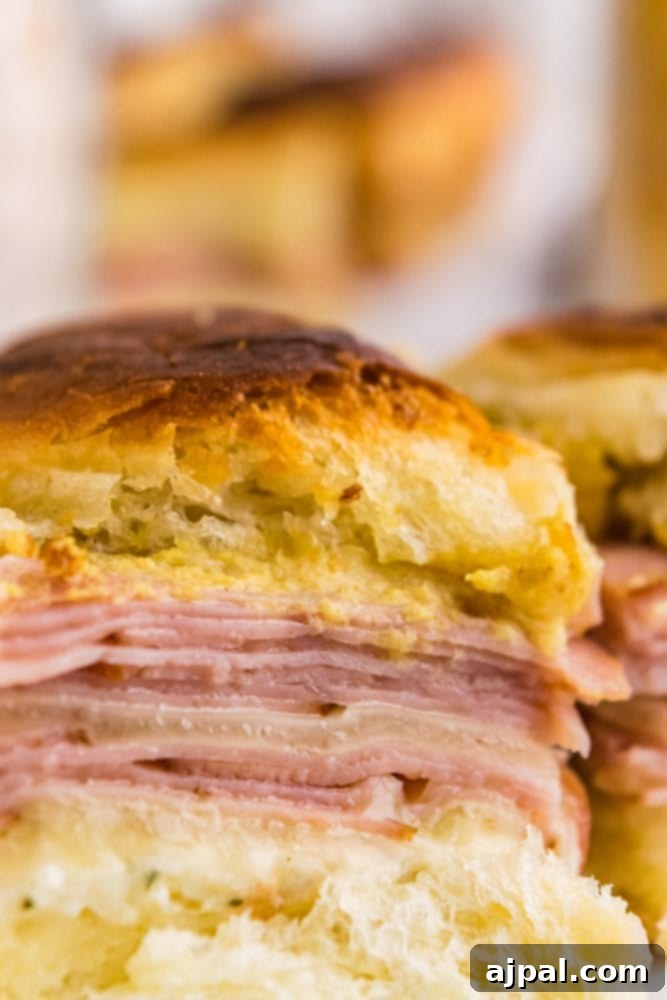 Close-up picture of a baked ham and cheese slider with melted cheese and golden-brown bun.