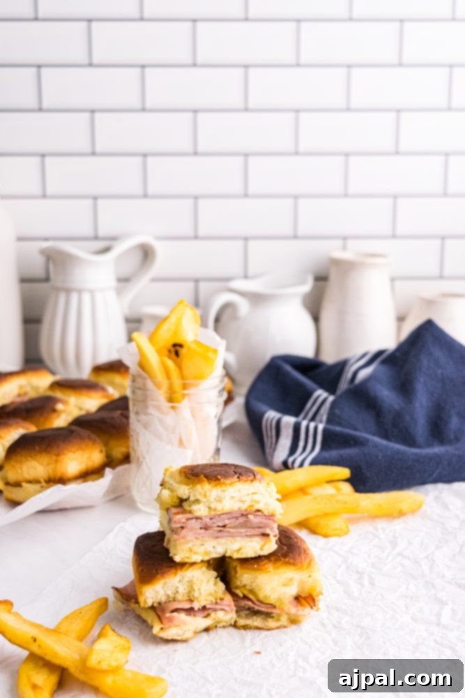 Picture of baked ham and cheese sliders on a white countertop with a blue towel and golden french fries in the background.