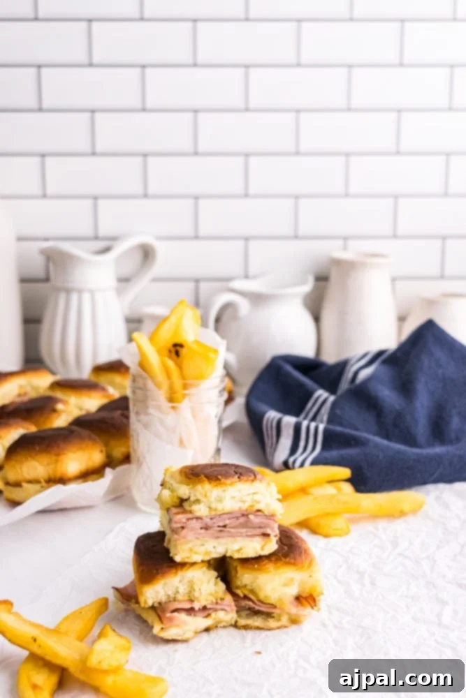 picture of ham and cheese sliders on a white countertop with blue towel and french fries in the background. 