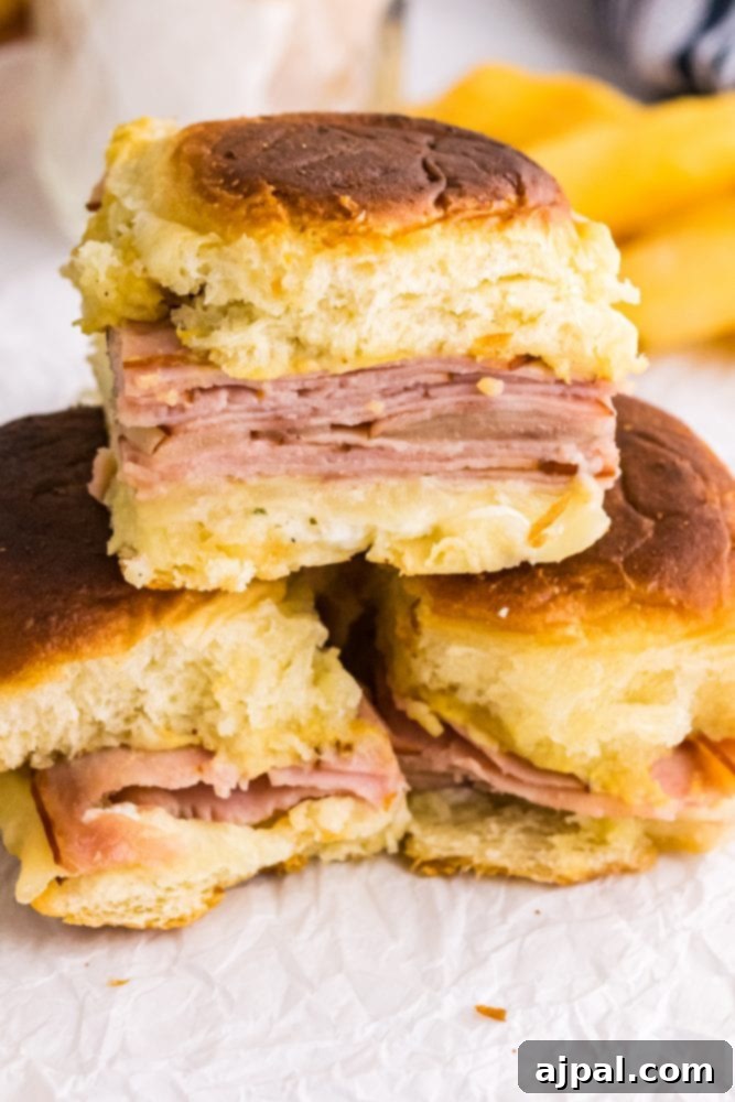 Picture of three ham and cheese sliders stacked on parchment paper, ready to serve.