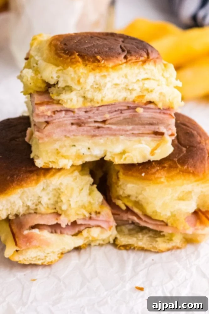 picture of three ham and cheese sliders stacked on parchment paper. 