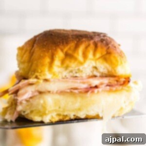 A baked ham and cheese sandwich being held up by a fork, showcasing its melted cheese and golden bun.