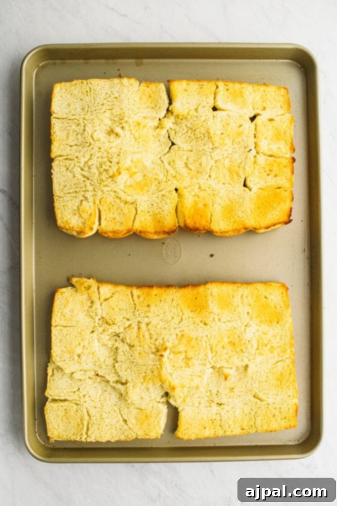 Picture of Hawaiian rolls laid out on a sheet pan with butter on them, ready for baking.