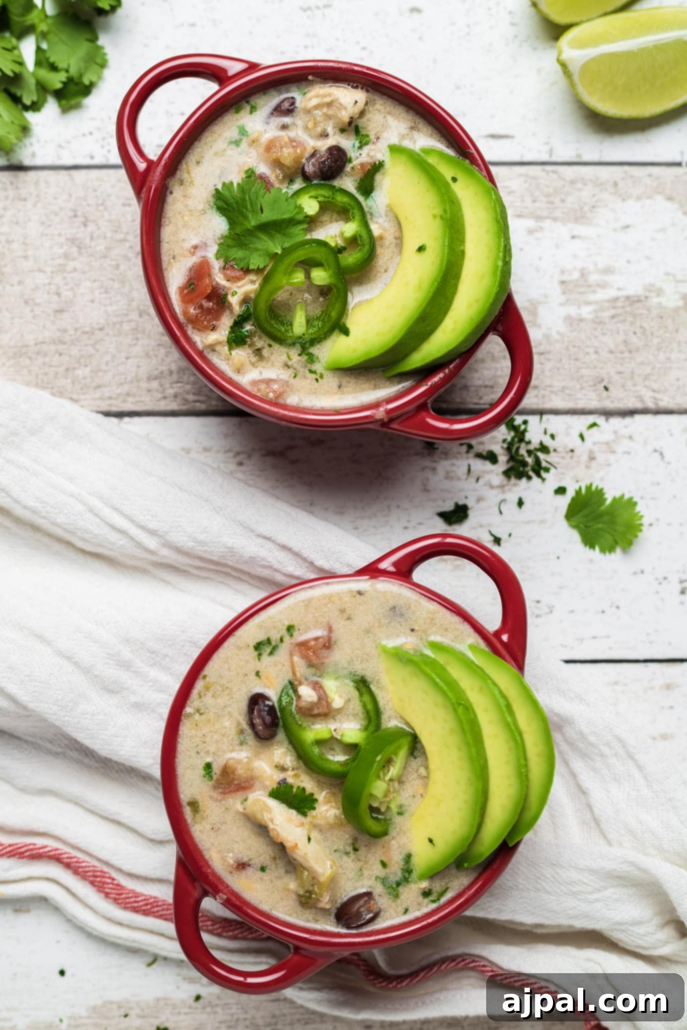 Easy chicken enchilada soup in two red bowls on a wooden table, garnished with fresh cilantro and avocado.