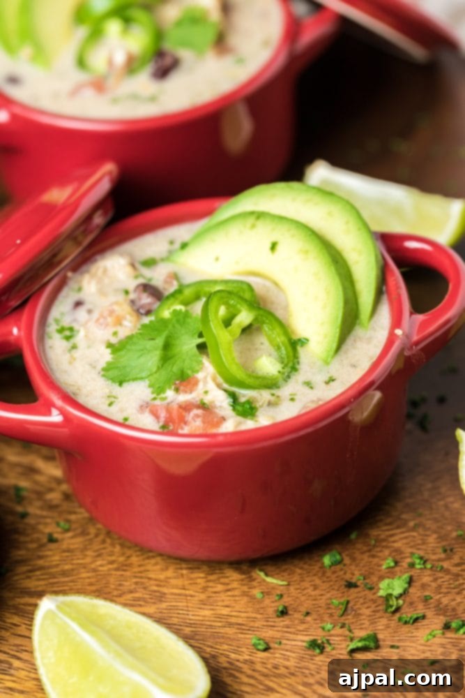 Two red bowls of creamy chicken enchilada soup, garnished with fresh avocado and lime slices, set on a rustic wooden surface.